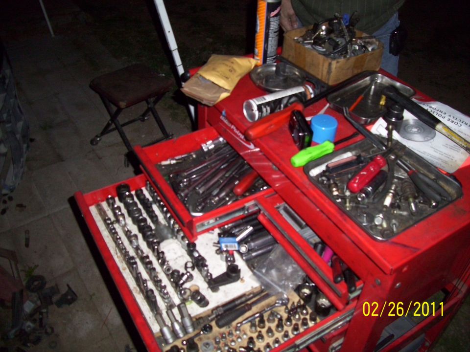 Red tool chest open with drawers full of sockets, wrenches, and spark plugs. A small stool is nearby
