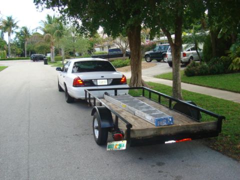 2002 Ford Crown Victoria - A white 2002 Ford Crown Victoria is seen from the rear, towing a trailer loaded with a ladder.
