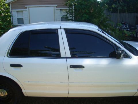 2002 Ford Crown Victoria - The side profile of a white 2002 Ford Crown Victoria sedan shows its tinted windows and black door handles.