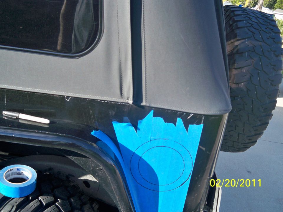 Black Jeep Wrangler rear quarter panel with blue tape, marker, and spare tire. Date stamp reads 02/20/2011