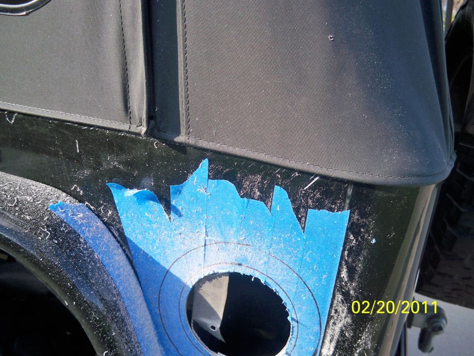 Black Jeep fender with blue tape marking a hole for modification