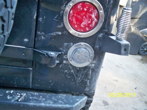1992 Jeep Wrangler - Close-up of the rear bumper and taillight assembly on a black Jeep Wrangler, showing the fuel filler cap and 'HI-OUT' text.
