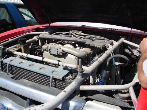 1992 Ford Taurus - The engine bay of a red vehicle is shown, with a roll cage and another blue vehicle visible in the background.