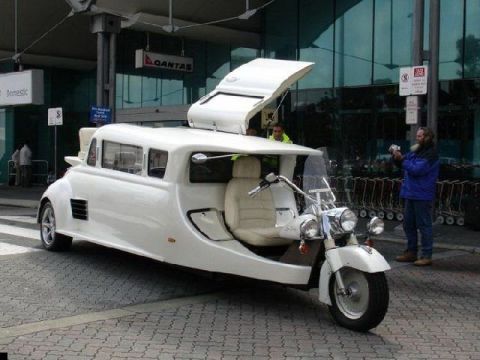 1981 Ford Bronco - A unique white trike resembling a limousine is parked outside an airport terminal.