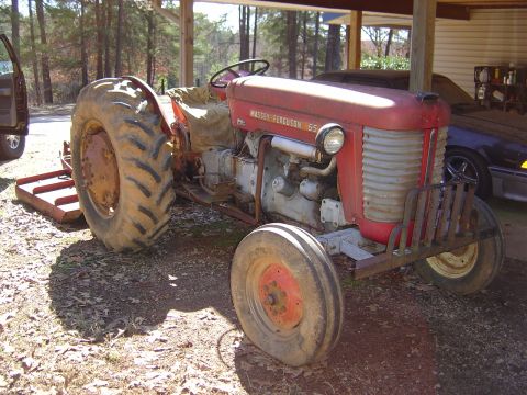 1986 Ford Bronco - Massey Ferguson 65 tractor with a flat front tire, parked under a shelter.