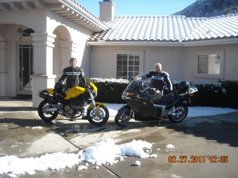 1965 Ford Mustang - Two men pose with their motorcycles in a driveway with snow on the ground.