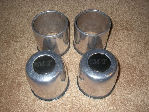 1990 Ford Bronco - Four polished aluminum wheel center caps, two showing the black M/T Mickey Thompson logo, arranged on carpet.