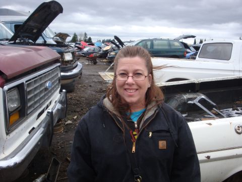 1989 Ford Bronco - A woman stands in a junkyard with several vehicles in the background.