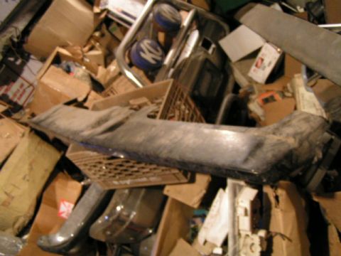 1979 Ford Bronco - A collection of automotive parts, including a bumper, are stored amongst cardboard boxes.
