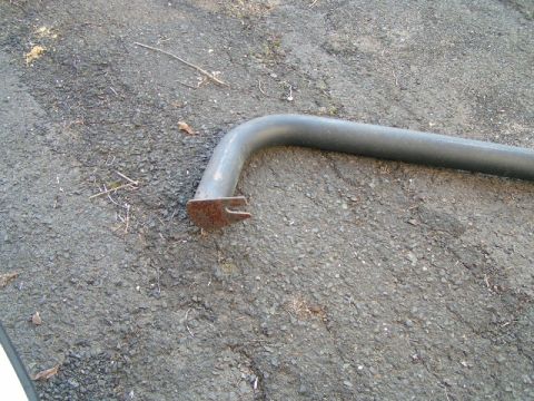 1979 Ford Bronco - A single gray metal pipe with a rusty mounting bracket lies on an asphalt surface. The registry claims it is from a 1979 Ford Bronco.