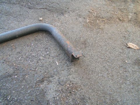 1979 Ford Bronco - A rusted metal pipe with a mounting bracket lies on an asphalt surface.