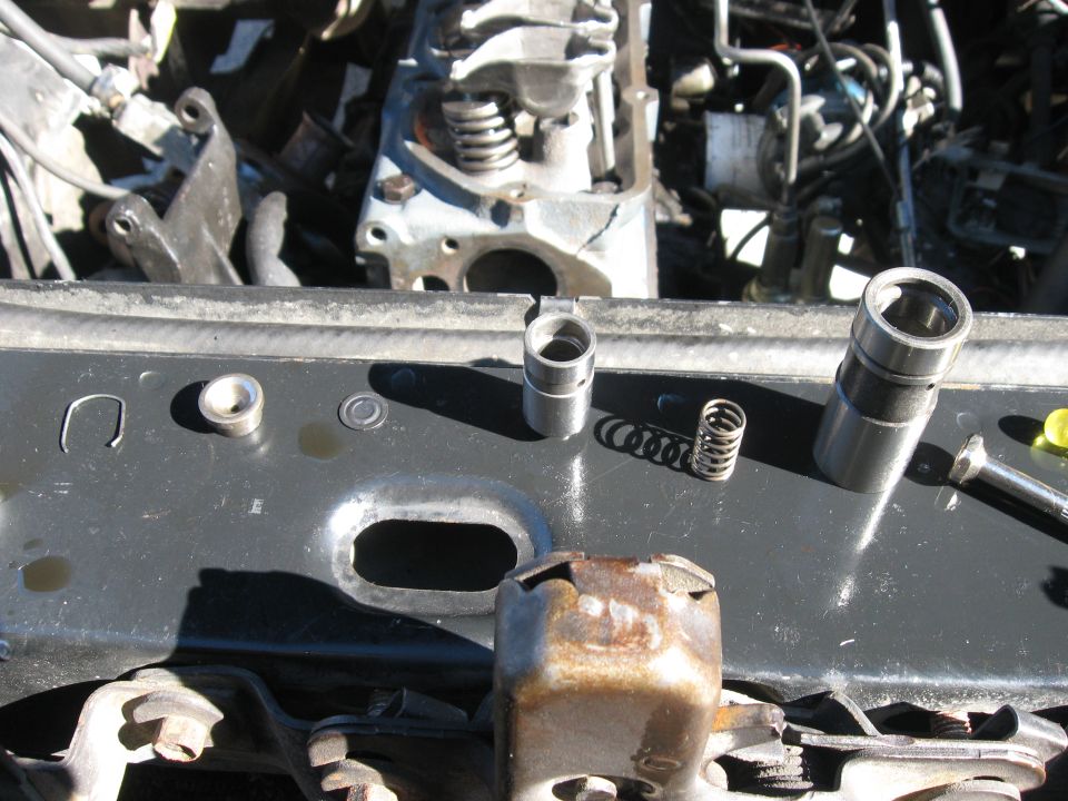 Engine lifters and springs on a black metal surface with engine components in the background