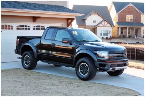 1990 Ford Bronco - A black Ford F-150 SVT Raptor pickup truck is parked in a driveway in front of a suburban home.