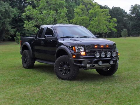 1990 Ford Bronco - A black Ford F-150 Raptor pickup truck is shown from the front 3/4 angle on a grassy field.