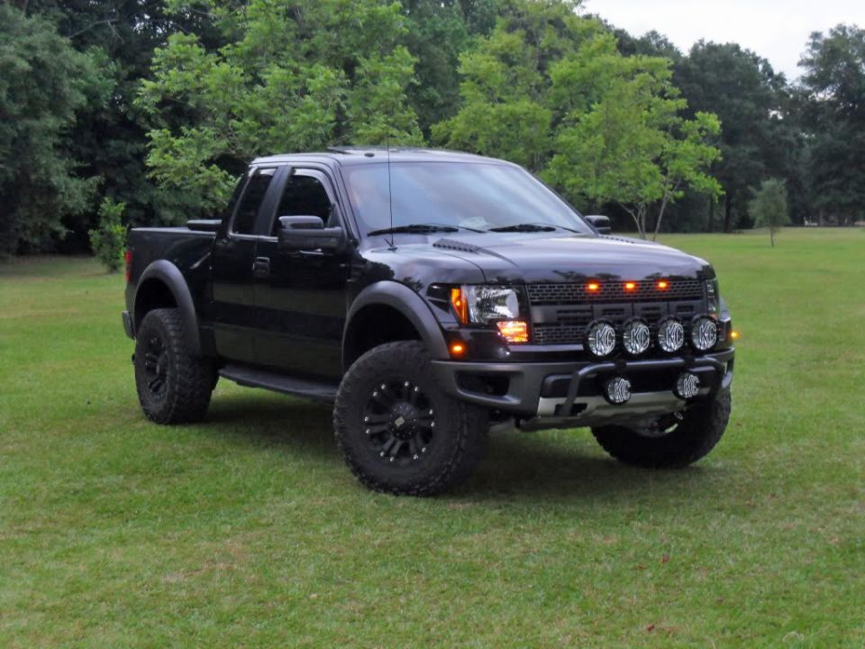Black lifted Ford pickup with KC off-road lights and black wheels on grass
