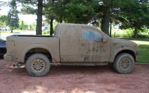 1990 Ford Bronco - A pickup truck covered in mud sits on a dirt road, with trees in the background.