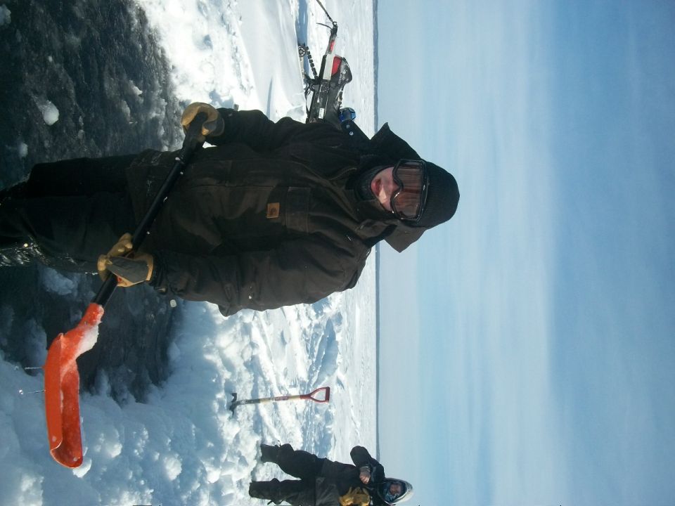 Two people in winter gear on a frozen surface with snowmobiles in the background