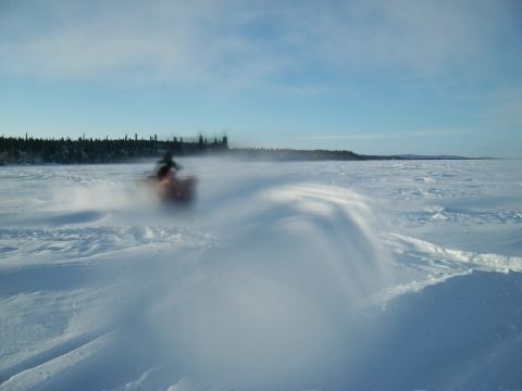 1986 Chevrolet Blazer - A snowmobile travels across a vast, snow-covered area under a bright blue sky.