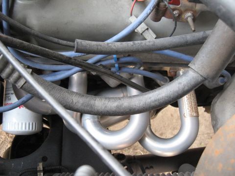 1994 Ford Bronco - Close-up of silver Bassani headers and blue spark plug wires in an engine compartment.