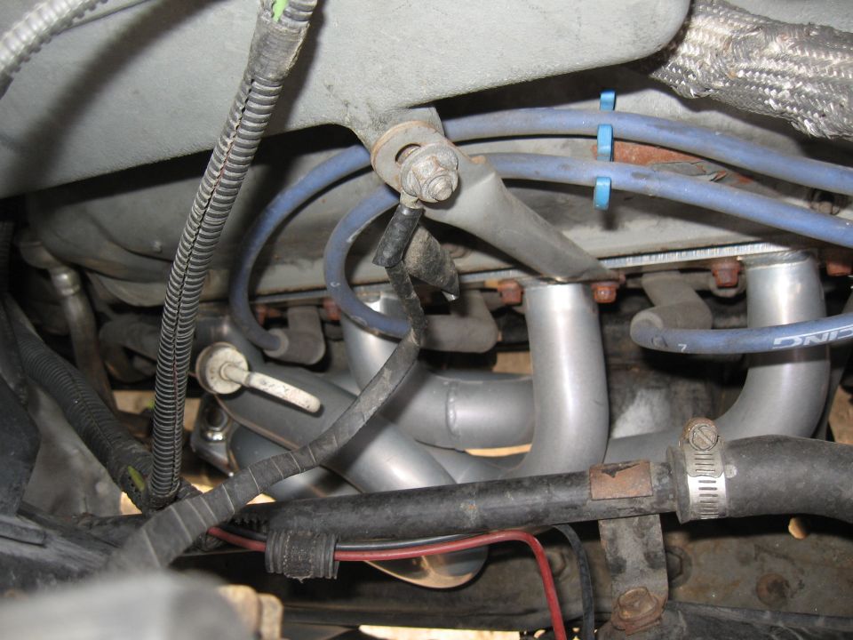 aftermarket exhaust headers installed on an engine, with blue spark plug wires and black hoses visible
