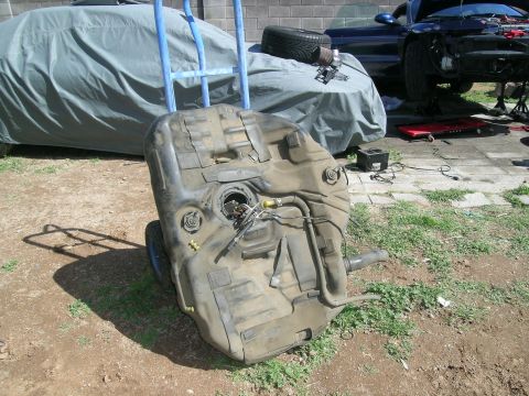 1995 Ford Probe - A removed fuel tank sits on a dolly in front of a car covered with a tarp and another car undergoing repairs.