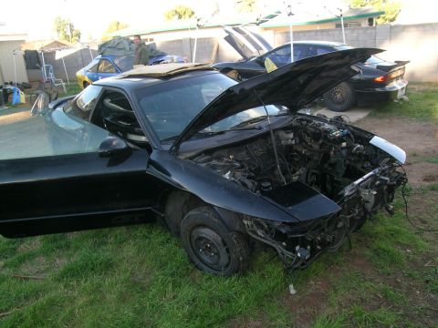 1995 Ford Probe - Two black coupes are parked on grass, one with its hood and door open, revealing its engine.