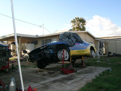 1995 Ford Probe - This 1995 Ford Probe is elevated on jack stands, revealing its blue and yellow racing livery with 'KELLY' text visible on the side.