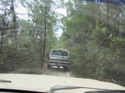 1990 Ford Bronco - A convoy of SUVs navigates a dusty, wooded trail, with the lead vehicle clearly visible.