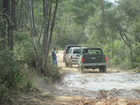 1990 Ford Bronco - Three SUVs navigate a muddy trail through a wooded area.