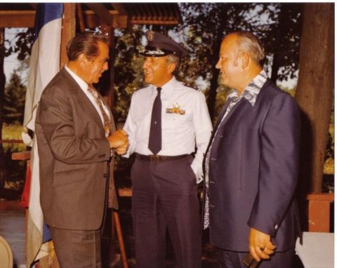 2003 Ford Crown Victoria - Three men, two in suits and one in a military uniform, converse outdoors near a flag.