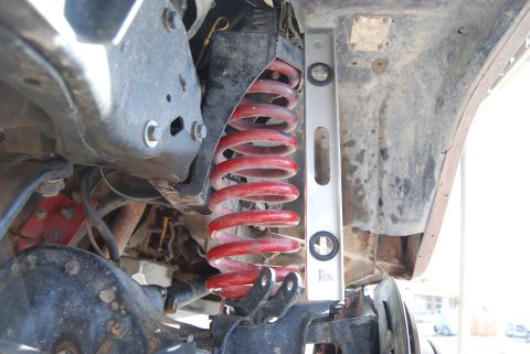 1982 Ford Bronco - A close-up view of a vehicle's suspension system, focusing on a red coil spring and a leveling tool.