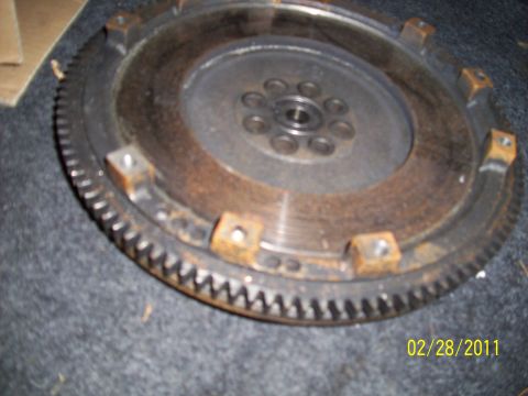 1995 Ford Probe - A close-up view of a rusty flywheel, showing its gear teeth and mounting bolt holes.