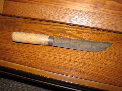 2010 Champion 188 - A rustic knife with a wooden handle and a weathered, rusted blade rests on a polished wooden surface.