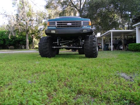 1978 Ford Bronco - A teal Ford truck with a lifted suspension and massive tires sits in a grassy yard.