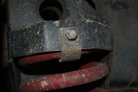 1982 Ford Bronco - This image shows a close-up view of a vehicle's suspension system, focusing on a coil spring and mounting bracket.