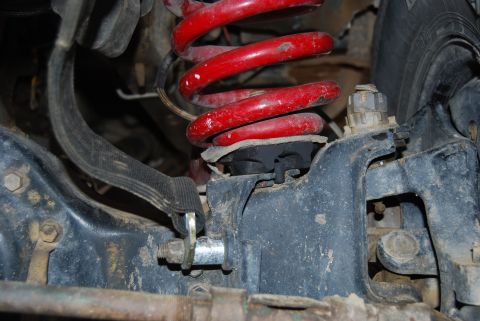1982 Ford Bronco - This image shows a close-up view of a vehicle's suspension, focusing on a red coil spring and surrounding mechanical parts.