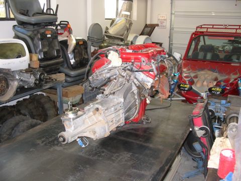1993 Ford Taurus - An engine and transmission assembly is displayed on a workbench, with a red vehicle visible in the background of the garage.