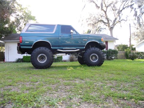1978 Ford Bronco - A lifted green Ford Bronco sits on a grassy lawn in front of a house.