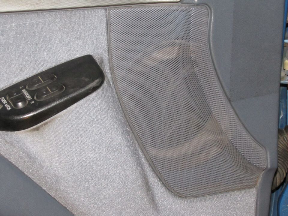 Gray interior door panel with black power window and lock controls and a textured speaker grille