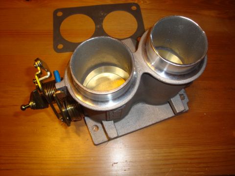1989 Ford Bronco - A dual throttle body assembly and gasket are shown on a wooden surface.