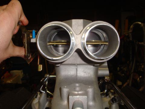 1989 Ford Bronco - A hand operates the linkage on a dual throttle body assembly, revealing the internal brass plates.