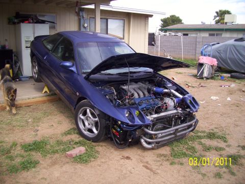 1995 Ford Probe - A blue 1995 Ford Probe is shown with its hood open, revealing the engine, and its front bumper removed.