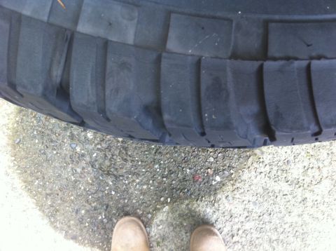 1990 Ford Bronco - A close-up view of a tire's tread pattern is shown, with two feet visible on the ground.