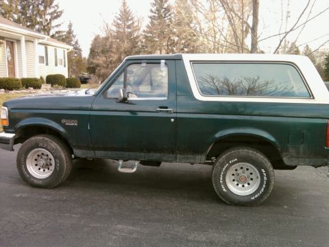 1993 Ford Bronco - A green 1993 Ford Bronco with a white removable top is parked on an asphalt surface.
