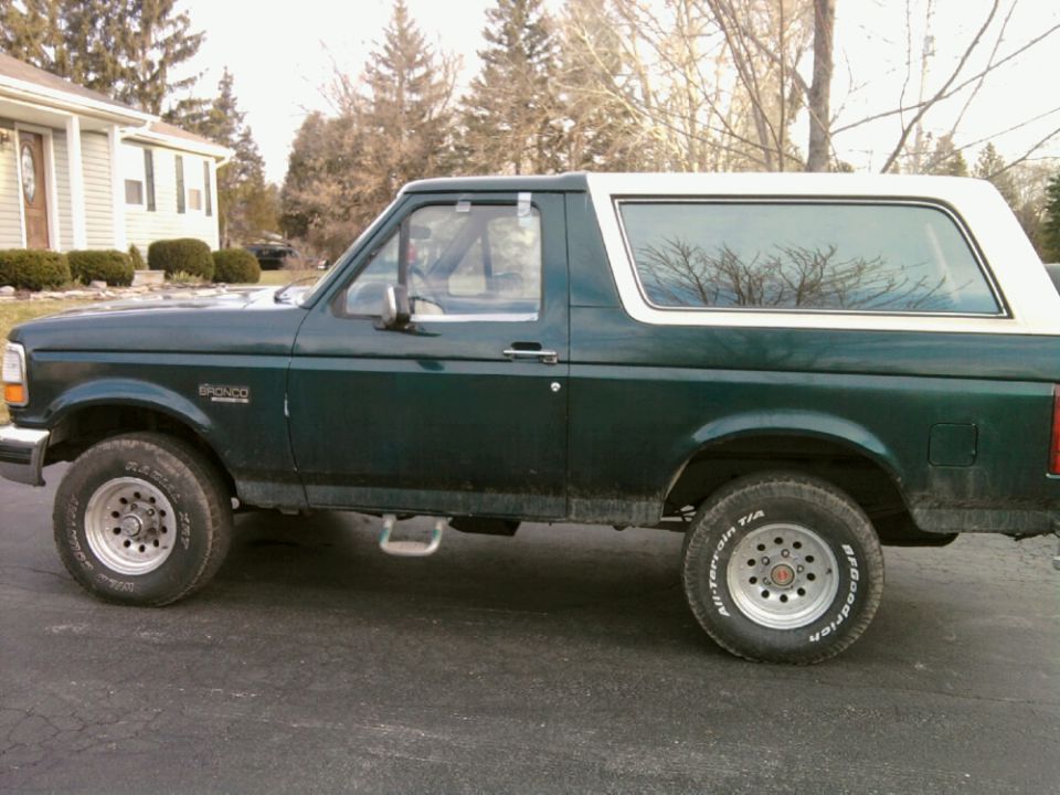 Green 1993 Ford Bronco side view, white top, silver wheels, on asphalt