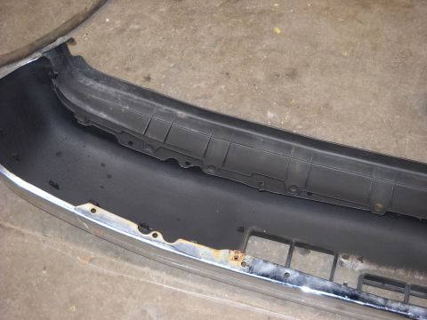 1993 Ford C-150 (Centurion Conversions) - Close-up of a front bumper, showing chrome and black plastic components with signs of rust.