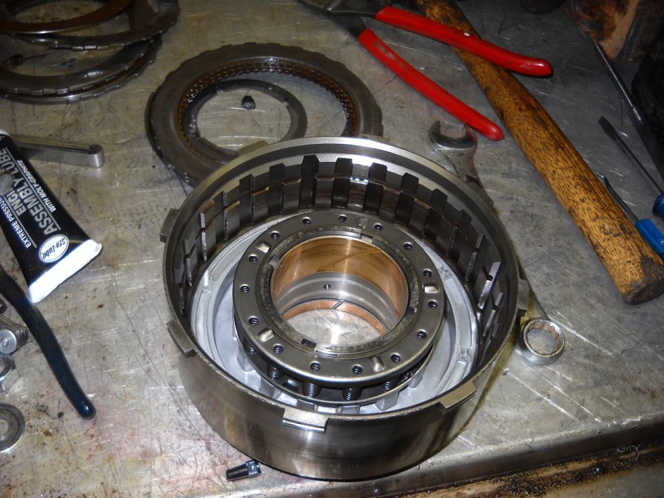 Disassembled automatic transmission drum with clutch plates and bearings. Tools and assembly lube are on the workbench