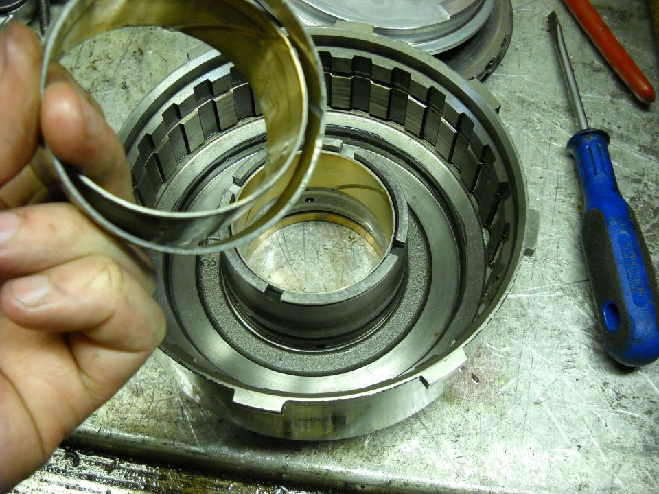 Transmission drum with a hand holding a metal ring over it. A blue screwdriver is to the right