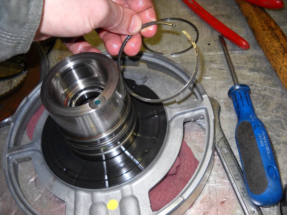 Hand holding broken metal ring over transmission component. Tools visible