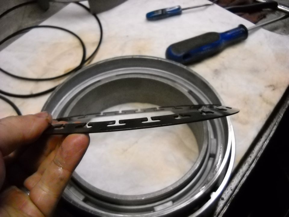 Hand holding a metal washer over a transmission drum with screwdrivers in the background